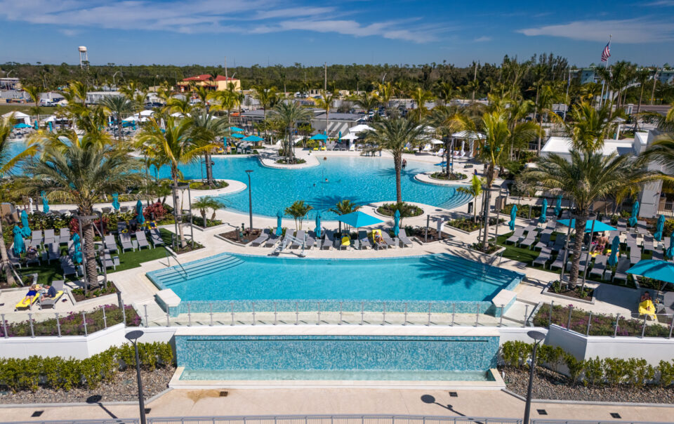 aerial view of a large hotel pool with sunbathers, tropical landscaping, glass railing, and cable railing
