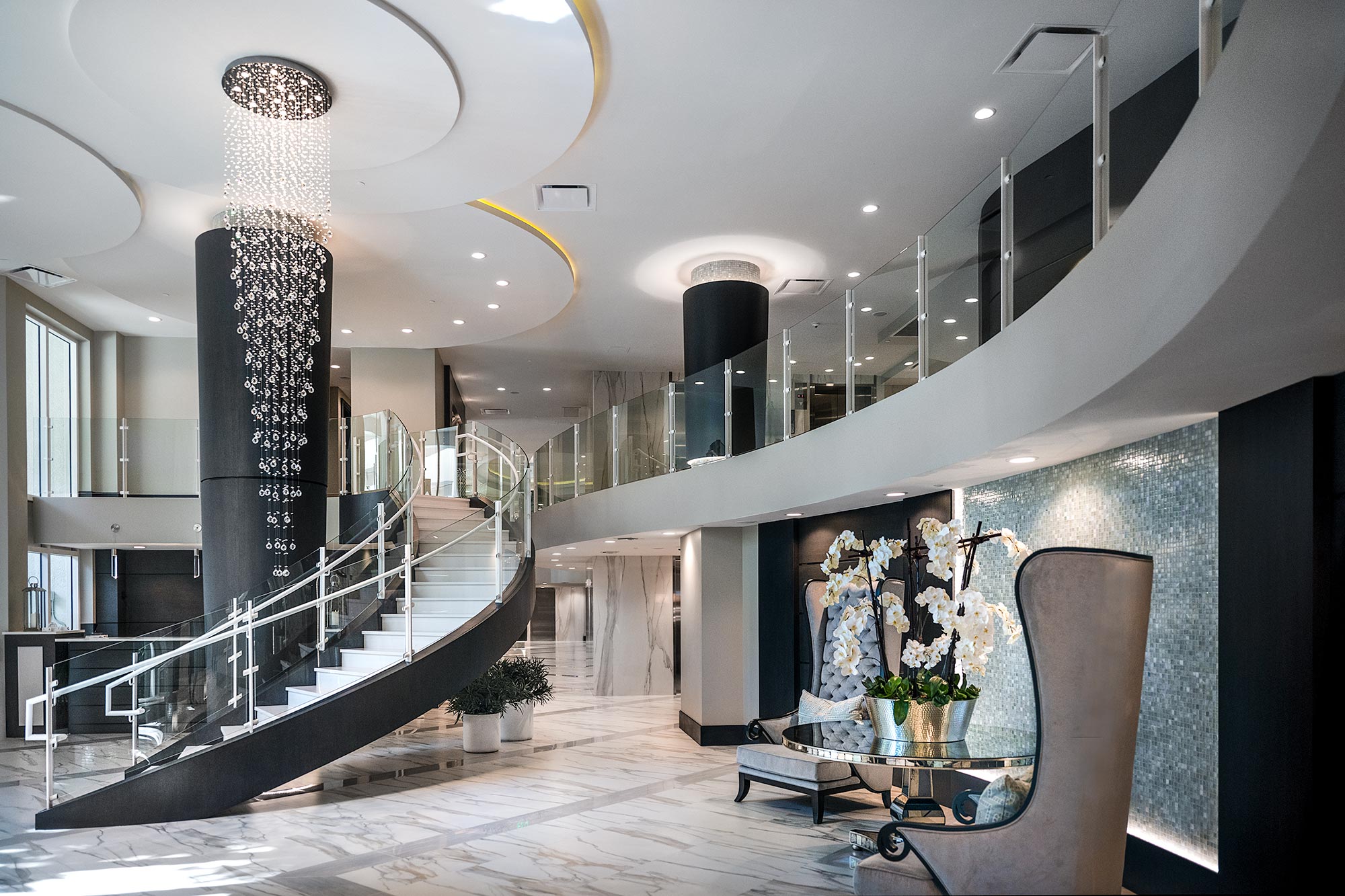 interior photograph of the luxury Seaglass condominium's lobby with a floating staircase, glass railing, and long crystal chandelier